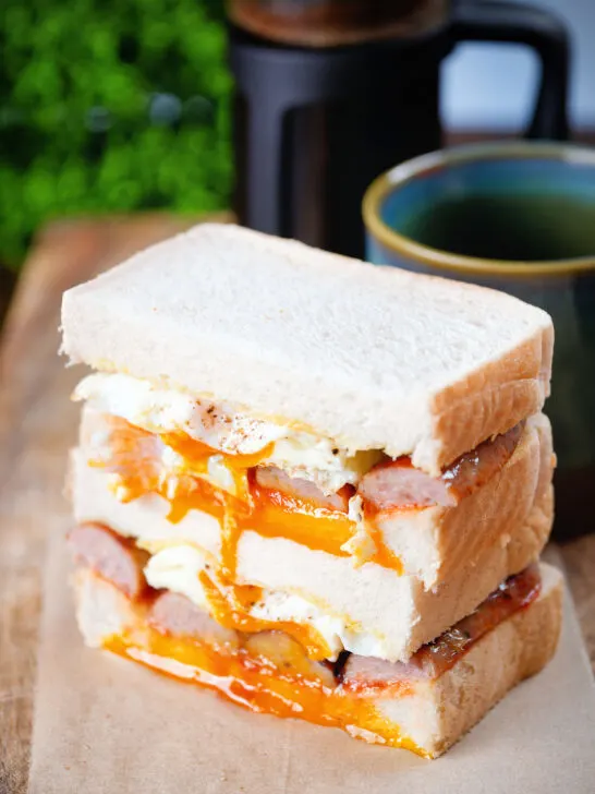 Simple sausage and fried egg breakfast sandwich with a runny yolk served with coffee.
