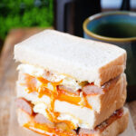 Simple sausage and fried egg breakfast sandwich with a runny yolk served with coffee.