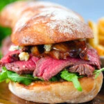 Close-up steak, stilton and caramelised onion sandwich served on ciabatta with french fries.