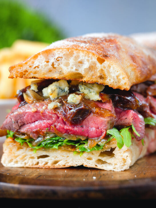 Cut in half, close-up steak, stilton, caramelised onion and rocket sandwich served on ciabatta.