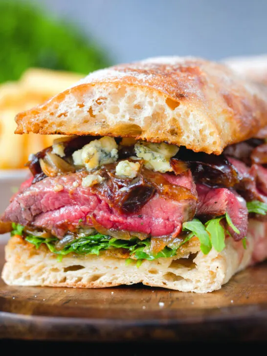Cut in half, close-up steak, stilton, caramelised onion and rocket sandwich served on ciabatta.