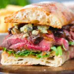 Cut in half, close-up steak, stilton, caramelised onion and rocket sandwich served on ciabatta.