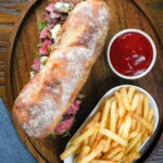 Overhead steak, stilton and caramelised onion sandwich served on ciabatta with french fries.