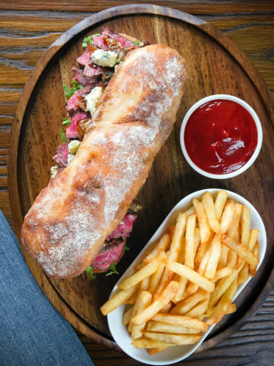 Overhead steak, stilton and caramelised onion sandwich served on ciabatta with french fries.