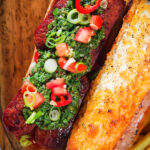 Overhead Argentinian-Influenced choripan sandwich with Spanish chorizo, chimichurri and salsa.
