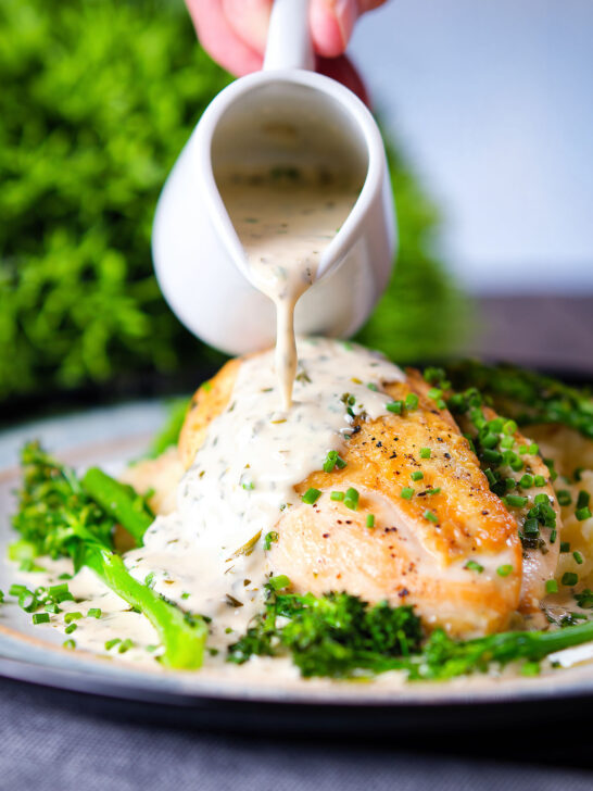 Creamy tarragon sauce being poured over chicken breast with celeriac mash and broccoli.