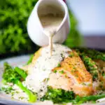Creamy tarragon sauce being poured over chicken breast with celeriac mash and broccoli.