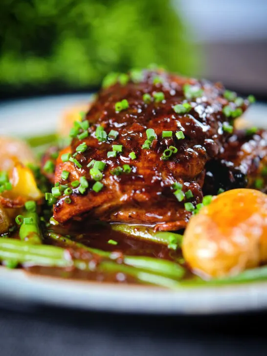 Close-up devilled chicken thighs served with roasted new potatoes, green beans and chives.