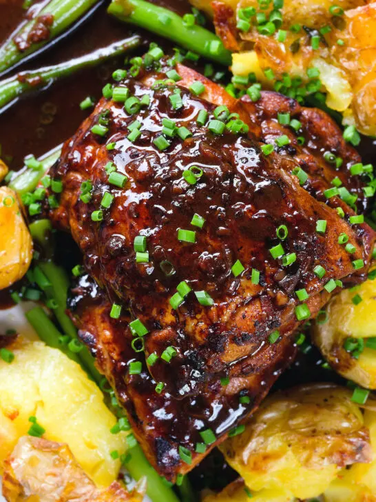 Overhead close-up devilled chicken thighs served with roasted new potatoes, green beans and chives.