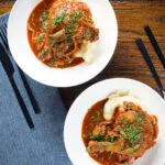 Overhead chicken chasseur or French hunters chicken served with mashed potato in two bowls.