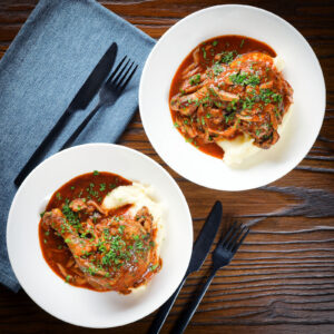 French chicken leg chasseur served with mashed potato in two bowls.