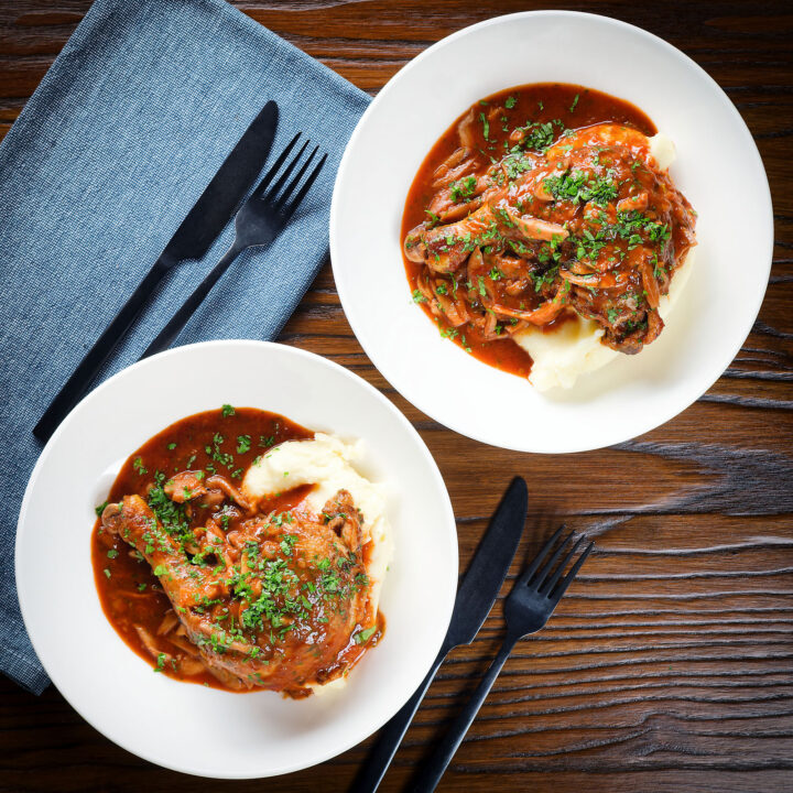 French chicken leg chasseur served with mashed potato in two bowls.