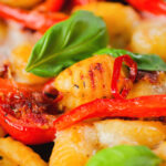 Close-up gnocchi tray bake with sun-dried and fresh tomatoes, mozzarella and pickled chilli.