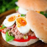 Pan bagnat (French tuna sandwich) with tomatoes, boiled egg and capers on a bread roll.