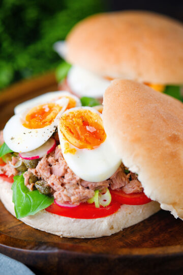 Pan bagnat (French tuna sandwich) with tomatoes, boiled egg and capers on a bread roll.