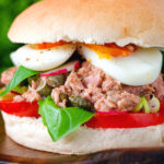 Pan bagnat (French tuna sandwich) with tomatoes, boiled egg, basil, radishes and capers.