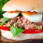 Pan bagnat (French tuna sandwich) with tomatoes, boiled egg, basil, radishes and capers.