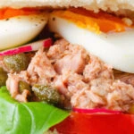 Close-up pan bagnat (French tuna sandwich) with tomatoes, boiled egg and capers on a bread roll.