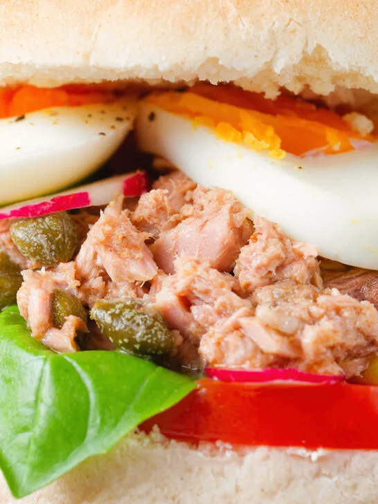 Close-up pan bagnat (French tuna sandwich) with tomatoes, boiled egg and capers on a bread roll.