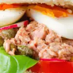 Close-up pan bagnat (French tuna sandwich) with tomatoes, boiled egg and capers on a bread roll.
