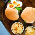 Overhead pan bagnat (French tuna sandwich) with tomatoes, boiled egg and capers on a bread roll.