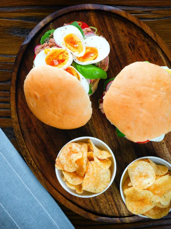Overhead pan bagnat (French tuna sandwich) with tomatoes, boiled egg and capers on a bread roll.