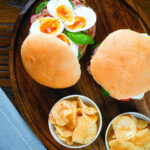 Overhead pan bagnat (French tuna sandwich) with tomatoes, boiled egg and capers on a bread roll.