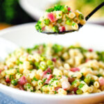 Italian pasta e piselli with peas, pancetta, mint, parsley and ditalini being eaten with a spoon.