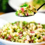 Italian pasta e piselli with peas, pancetta, mint, parsley and ditalini being eaten with a spoon.