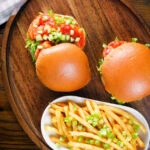 Overhead prawn sandwich with a bloody Mary sauce and celery on a brioche bun served with French fries.