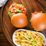 Overhead prawn sandwich with a bloody Mary sauce and celery on a brioche bun served with French fries.