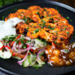 Roasted tandoori cauliflower steak with kachumber salad, mango chutney and mint raita.