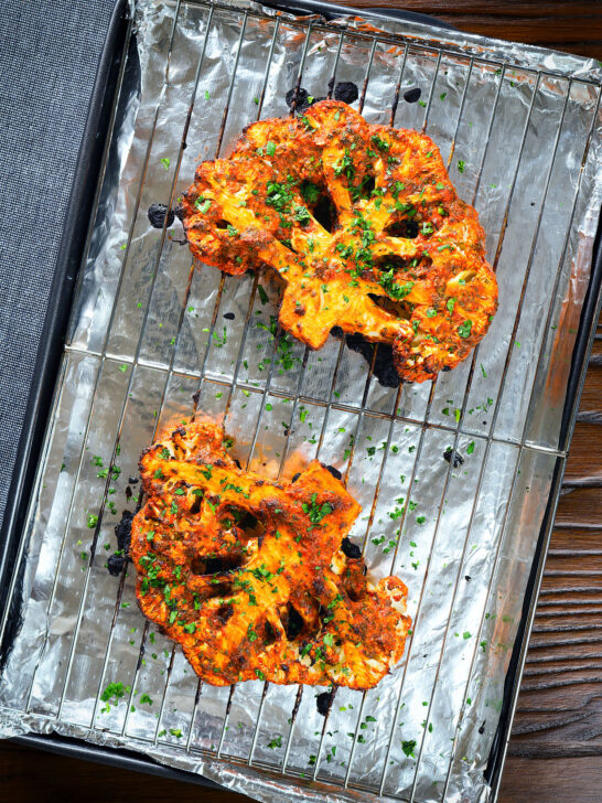 Roasted tandoori cauliflower steaks on a baking tray.