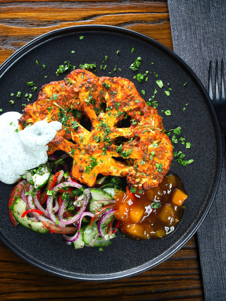 Overhead roasted tandoori cauliflower steak with kachumber salad, mango chutney and mint raita.