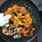 Overhead roasted tandoori cauliflower steak with kachumber salad, mango chutney and mint raita.