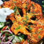 Overhead close-up roasted tandoori cauliflower steak with kachumber salad, mango chutney and mint raita.