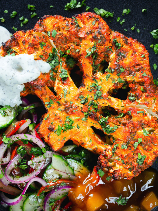 Overhead close-up roasted tandoori cauliflower steak with kachumber salad, mango chutney and mint raita.