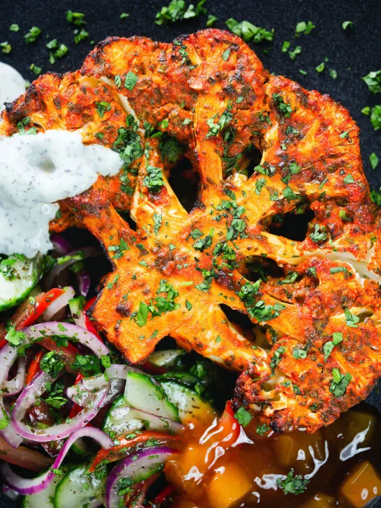 Overhead close-up roasted tandoori cauliflower steak with kachumber salad, mango chutney and mint raita.