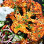 Overhead close-up roasted tandoori cauliflower steak with kachumber salad, mango chutney and mint raita.