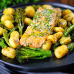 Salmon fillet tray bake with pesto, green veggies and gnocchi served on a black plate.