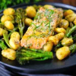 Salmon fillet tray bake with pesto, green veggies and gnocchi served on a black plate.