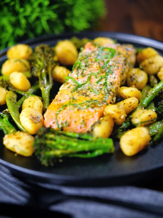 Salmon fillet tray bake with pesto, green veggies and gnocchi served on a black plate.