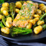 Salmon fillet tray bake with pesto, green veggies and gnocchi served on a black plate.