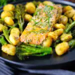 Salmon fillet tray bake with pesto, green veggies and gnocchi served on a black plate.