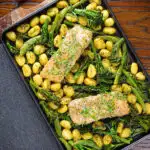 Overhead salmon fillet traybake with pesto, green veggies and gnocchi served on a sheet pan.