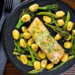 Overhead salmon fillet traybake with pesto, green veggies and gnocchi served on a black plate.
