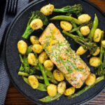 Overhead salmon fillet traybake with pesto, green veggies and gnocchi served on a black plate.