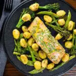 Overhead salmon fillet traybake with pesto, green veggies and gnocchi served on a black plate.