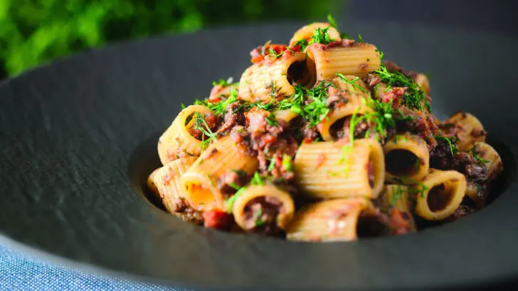 Sardine pasta Bolognese or ragu garnished with basil served in a black bowl.