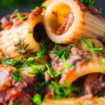 Close-up sardine and tomato pasta Bolognese or ragu garnished with fresh basil.